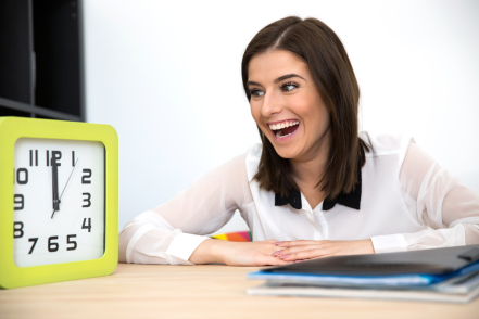 Surprised businesswoman sitting at the table and looking on the clock